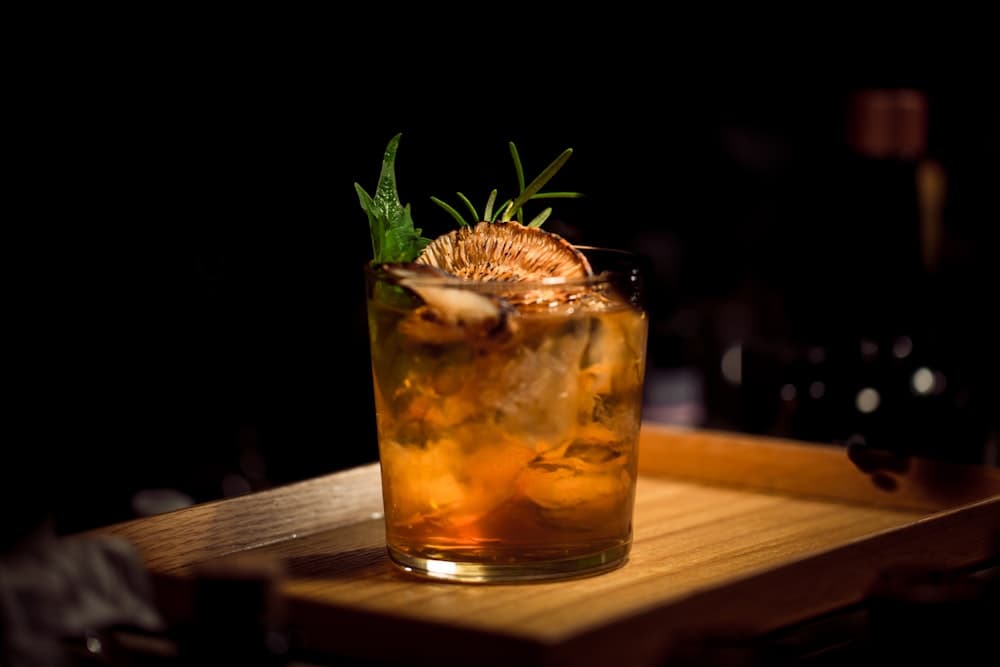 Glowing handcrafted cocktail in crystal rocks glass with orange crown